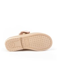 Suela de un zapato infantil beige con textura antideslizante, tamaño 25, etiqueta "Hecho en España" y un lazo decorativo en la parte superior.