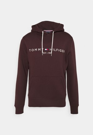 Dunkelbrauner Hoodie mit Fronttasche, weißen Kordeln und dem "Tommy Hilfiger Est. 1985" Logo in Weiß sowie Details in Rot und Blau.