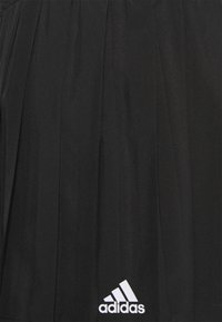 Mustan urheiluhameen ohut kangas, jossa on laskostettu muotoilu. Alareunassa valkoinen Adidas-logo vasemmalla puolella.