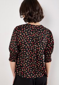 Zwarte bloes met een bloemenprint van rode en roze bloemen, korte pofmouwen met gathered cuffs en een gesmokte achterkant. Lichtgewicht stof.
