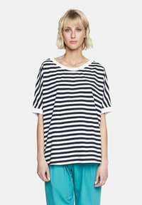 Czarnobiała, paskowana koszula z krótkim rękawem i szerokim dekoltem z białym wykończeniem, noszona z spodniami w kolorze akwamarynowym, prezentującymi luźny krój.