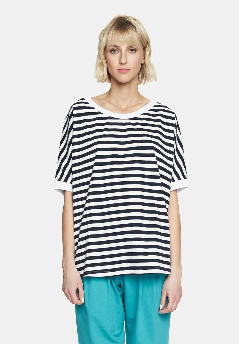 Czarnobiała, paskowana koszula z krótkim rękawem i szerokim dekoltem z białym wykończeniem, noszona z spodniami w kolorze akwamarynowym, prezentującymi luźny krój.