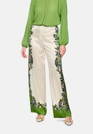 Wide-leg cream pants with green floral border patterns worn with a long-sleeve green blouse and cream pointed loafers with gold buckles.