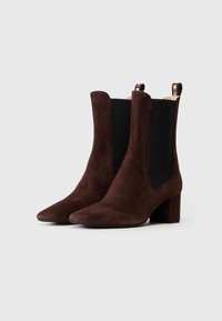 Paar pruuni seedermännipuidust ankle boots'id, millel on plokk-kandid ja mustad elastsed külgpaneelid heledal taustal.
