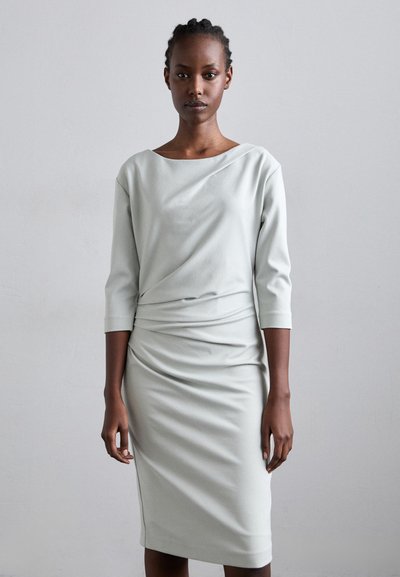 Vestido gris claro hecho de una tela suave, con un escote barco, mangas tres cuartos y un diseño drapeado con una silueta ajustada.