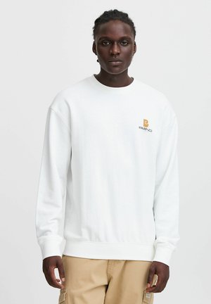 Sudadera blanca de manga larga, con cuello redondo y puños de canalé. Presenta un pequeño logo en el pecho en marrón y una textura sutil.