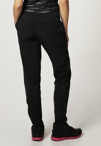 Black athletic pants with a smooth texture and a fitted design. Features an elastic waistband and tapered legs, paired with black shoes.