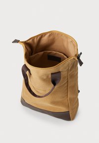 Canvas tote bag in mustard yellow with a brown leather base. Interior lined with light fabric; features dual brown handles and zipper closure.