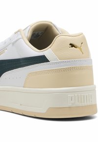 Hvide lædersneakers med en teal-stribe, beige detaljer og en struktureret bagside. Har en markant hvid sål og guldfarvet logo-detaljer.
