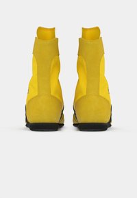 Yellow ankle boots with a smooth suede texture, elastic side panels, and black rubber soles, showcasing a sleek, modern design.