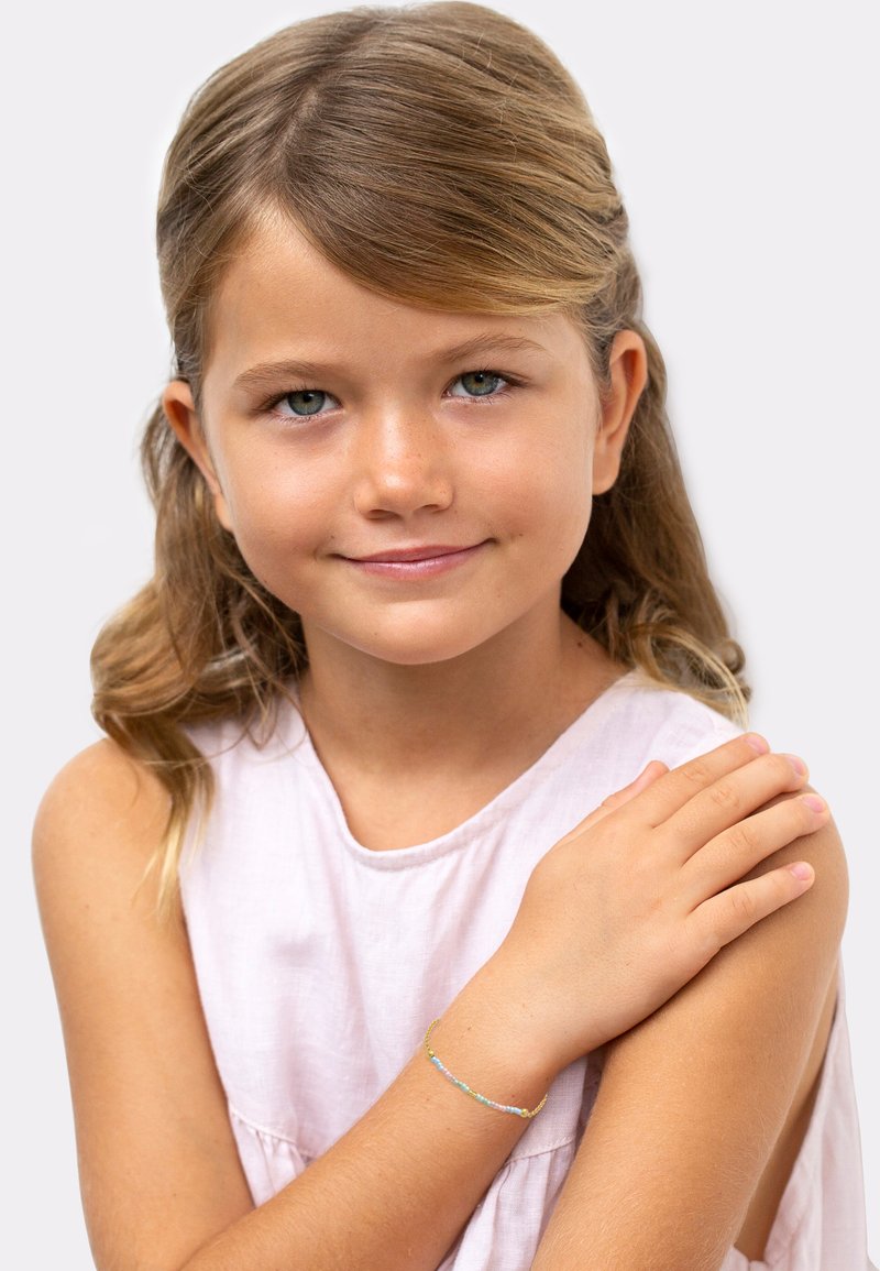 Une jeune fille portant un haut sans manches rose avec un bracelet en perles multicolores à son poignet. Le bracelet présente différentes couleurs pastel.