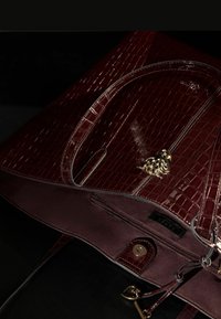 Geantă bordou cu un model embosat de crocodil, accente argintii și un charm decorativ de culoare aurie, având un buzunar cu fermoar și închidere magnetică.