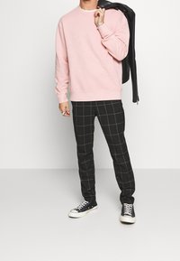 Rosa bomullströja med rund halsringning; svarta rutiga byxor med gula accenter; svarta sneakers med vita snören; läderjacka slängd över axeln.