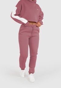 Sudadera cortada con capucha en color malva y mangas blancas, combinada con pantalones de chándal malva a juego. Tela suave y detalle de cintura con cordón.