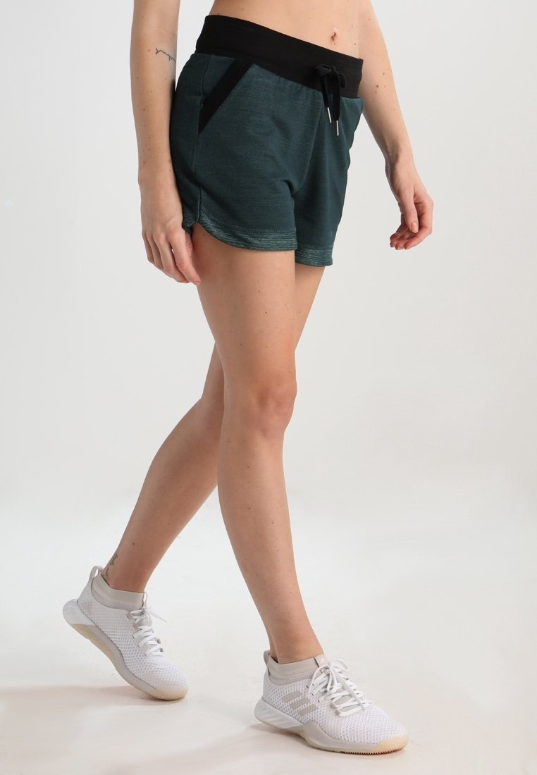 Tmavě modré sportovní šortky s černým pasem, detailem na šňůrku a bočními kapsami. V kombinaci s bílými texturovanými sportovními botami.