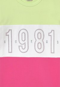 T-shirt med kortærmer, der har en mintgrøn top sektion, hvid midtersektion med rhinestone-nummeret "1981" og en lys pink bundsektion.