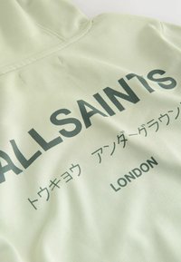 Lysegrøn hættetrøje med "ALLSAINTS," japanske tegn og "LONDON" trykt i mørkegrøn på brystområdet.