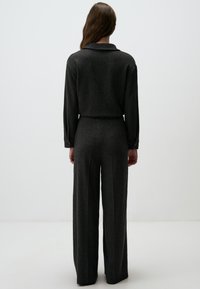 Ensemble deux pièces gris à côtes avec des manches longues et un pantalon à jambes larges. Le tissu présente un motif texturé, et il y a des détails de boutons sur les manches.