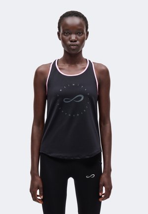 Mujer de pie mirando al frente, lleva una camiseta sin mangas negra con ribete rosa y leggings negros, ambos con un símbolo de infinito.