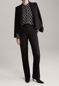 Black tailored blazer over a black and white patterned blouse, paired with high-waisted black trousers and pointed-toe heels.