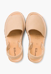 Beżowe skórzane sandały z zaokrąglonym noskiem, tylnym paskiem i białym przeszyciem. Gładka tekstura z płaską podeszwą, oznaczona detalami rozmiaru i marki.