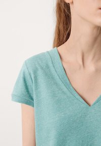 Mintgrünes V-Ausschnitt-T-Shirt aus weichem, leichtem Stoff; kurze gerollte Ärmel; dezente melierte Textur. Keine Muster oder Verzierungen.