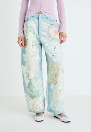Lichtblauwe denim broek met een brede pijp, voorzien van patchworkontwerpen in pastelkleuren en bloemenpatronen. Gecombineerd met roze flats.