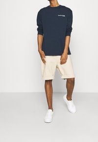 Long-sleeve navy t-shirt with white logo, paired with beige shorts and white sneakers. Simple design with rolled shorts.