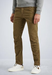 Chinos caqui con corte ajustado, que presentan un tejido de algodón texturizado, bolsillos en ángulo y un sutil detalle de costura. Combinados con zapatillas blancas.