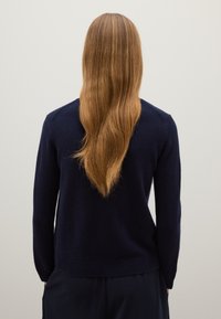 Marineblauer Pullover aus weichem Stoff, mit Rundhalsausschnitt und gerippten Bündchen. Die Rückansicht zeigt eine lockere Passform ohne sichtbare Muster.