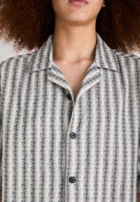 Camicia button-up realizzata in un tessuto strutturato e a righe in grigio chiaro e scuro. Presenta un colletto da campeggio e bottoni scuri.