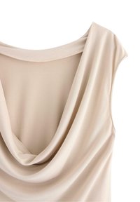 Beige ærmeløs top med draperet cowl-udskæring, glat stof og blød tekstur, med overlapping af lag, der skaber visuel interesse.