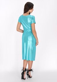 Akvaarinsininen satiini Mekko lyhyillä hihoilla, istuva vyötärö ja tuulen pieksu, joka ulottuu keskikalkkiin. Korostaa mustat korkokengät höyhenyksillä.