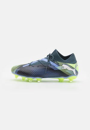 Scarpa da calcio di colore blu scuro e verde con una superficie texturizzata. Presenta un logo Puma distintivo e lacci angolati per una vestibilità aderente.