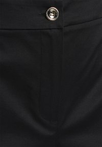 Svart tyg i närbild med en slät textur, sidoficka och en silverfärgad knappdetalj nära midjan.