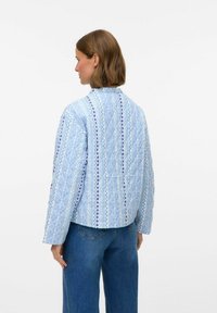 Vadderad blå jacka med mönstrad design som har zigzag- och stjärnmotiv. Rund krage, långa ärmar och en boxig passform. Jeanel.