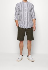 Camicia a righe grigia e bianca, abbinata a pantaloni corti verde oliva. Il modello indossa sneakers bianche con dettagli neri.
