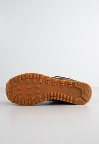 Semelle d'une chaussure marron avec des sculptures profondes et un logo de marque, affichée à plat sur une surface blanche sur fond uni.