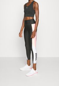 Czarny sportowy biustonosz i legginsy z wysokim stanem z różowymi i białymi panelami, z logo Puma oraz gładką, elastyczną fakturą materiału.