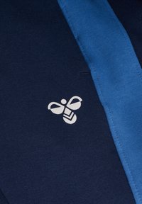 Marineblåt stof har en central blå stribe og et hvidt bi-grafik. Designet inkluderer en glat tekstur og syede detaljer.