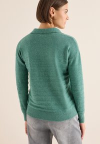 Grüner gestrickter Pullover mit strukturiertem Muster, ausgestattet mit einem gerippten Kragen und Ärmelbündchen. Weiches Material mit lockerer Passform und leicht abgerundetem Saum.