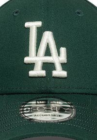 Gorra de béisbol verde con un logo bordado en blanco "LA" en la parte frontal. Incluye una etiqueta circular que dice "9FORTY AJUSTABLE."