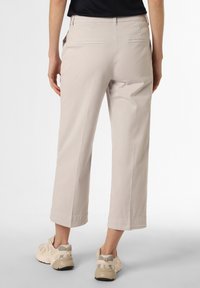 Pantalons cropped beige clair avec une texture lisse et deux poches arrière. Portés avec des baskets de couleur claire. Présentent un design simple et ajusté.