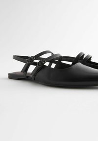 Czarne płaskie buty z ostro zakończonym noskiem, wykonane z gładkiego materiału. Posiadają trzy cienkie regulowane paski z okrągłymi klamrami.