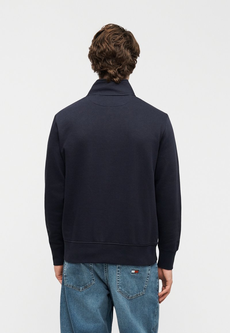 Felpa blu navy con collo alto, polsini e orlo a costine. Il tessuto sembra morbido; presenta un design semplice senza loghi o motivi visibili.