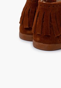 Brązowe botki zamszowe z frędzlami, miękką teksturą i zaokrąglonymi podeszwami dla wygody. Posiadają perforowane akcenty na górze.