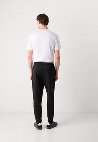 Svarta joggerbyxor med smal passform, elastisk midja och sidoficka, tillsammans med en enfärgad vit t-shirt med kort ärm och mörka skor.