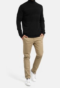 Svart stickad polotröja med texturerade ränder, ihop med ljusbeige chinos och vita sneakers. Enkelt design, åtsittande siluett.