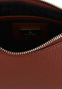 Interior de bolso de cuero marrón con acabado texturizado, cremallera dorada y forro negro con patrón. Cuenta con una etiqueta de la marca en el interior.