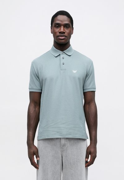 Πολο μπλούζα σε ήπιο πράσινο χρώμα, κατασκευασμένη από μαλακό υλικό, με γιακά, τρία κουμπιά και ένα μικρό λογότυπο στη θ胸.